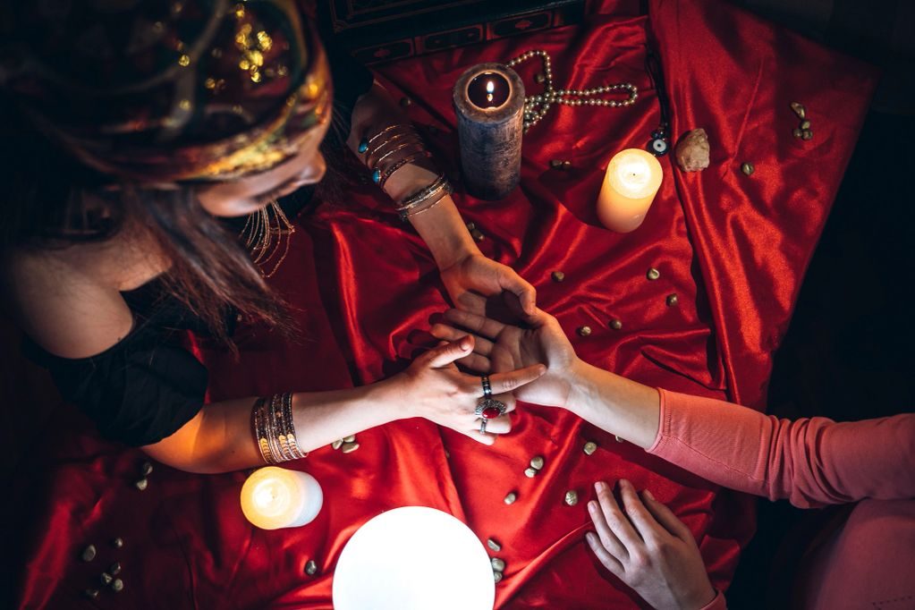 A psychic reading a client's palm by candlelight over red silk.